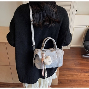 Detail of light gray textured crossbody bag with plush bear charm and long shoulder strap