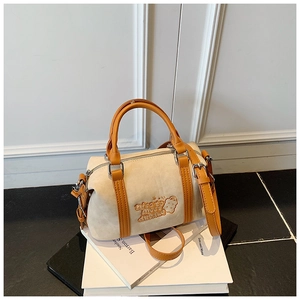 Detail der beigen Boston-Tasche mit orangefarbenen Ledergriffen und Cartoon-Stickerei