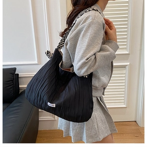 Détail d'un sac cabas plissé noir avec bandoulière rayée et étiquette tissée chic