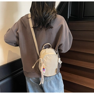 Detail of a beige nylon crossbody bag with dual zippers and decorative charm accessory