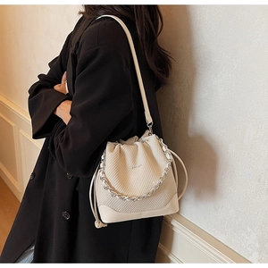 Detail of cream bucket bag with rhombus texture, silver chain, and drawstring closure