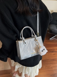 Silver metallic crossbody bucket bag with crinkle texture and plush eye pendant on model
