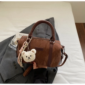 Brown Boston bag with pleated texture, plush bear charm, on a grey blazer setting