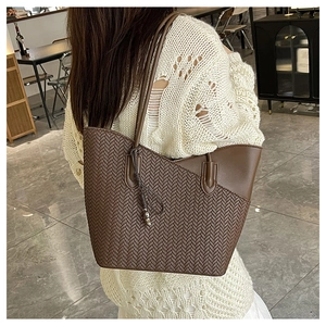 Close-up of brown woven tote bag with smooth leather trim and decorative tassel detail