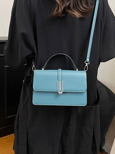 Blue leather crossbody bag with white stitching and silver hardware on a black coat model