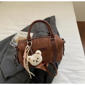 Detail of brown pleated shoulder bag with bear pendant and leather handle on soft bedding