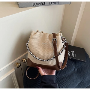 Detail of beige woven bucket bag featuring brown leather trim and silver chain handle