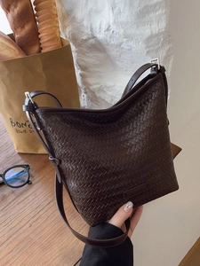 Dark brown woven leather bucket bag with adjustable strap on a French-style wooden table