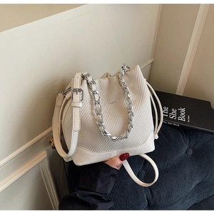 Close-up of a woven cream bucket bag featuring silver chain handle and leather strap