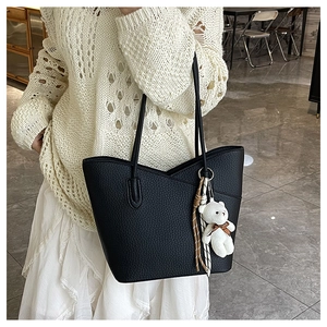Detail der schwarzen Tote Bag mit Litschi-Struktur und weißem Bär-Anhänger auf der Schulter