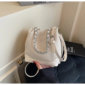 Close-up of cream bucket bag with woven texture, metal chain handle, and leather strap