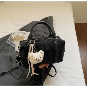 Detail of black pleated Boston bag with soft plush bear charm and adjustable strap