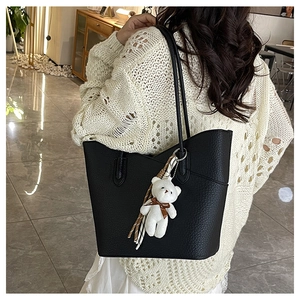 Detailansicht der schwarzen Tote Bag mit Lederstruktur und weißem Bär-Anhänger