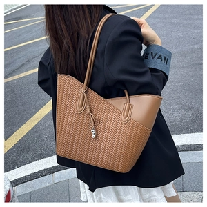 Detail of a brown tote bag featuring a woven patchwork design and heart charm accessory