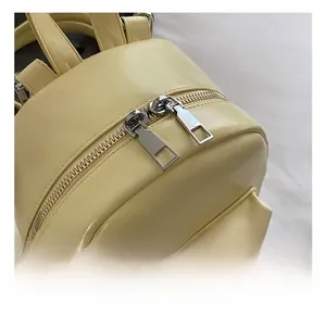 Detailed macro view of smooth dual silver zippers on a light yellow leather mini backpack