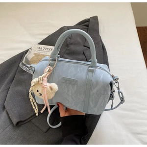Detail of light blue textured leather pillow bag with plush bear charm and strap