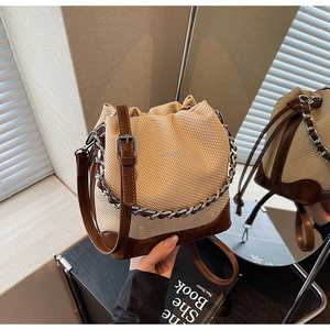 Detail view of woven bucket bag with brown leather trim and silver metal chain handle
