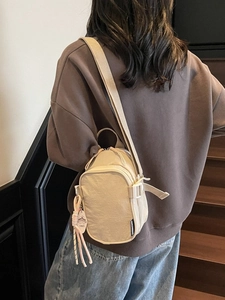 Minimalist beige nylon crossbody bag with zipper compartments and vintage charm accessory