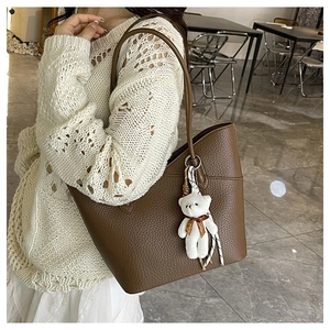Detail einer braunen Shopper-Tasche mit Kieselleder-Textur und süßem weißem Bären-Anhänger