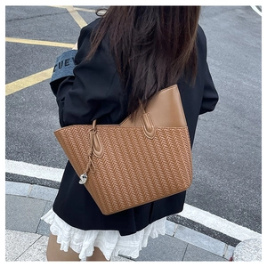 Street style shot of a vintage brown woven leather tote bag with a silver letter charm