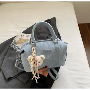 Detail of light blue Boston bag with pleated texture, handles, and a cute teddy bear charm