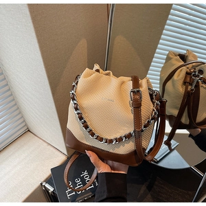 Detailed view of the woven textured bucket bag with leather trim and metal chain decor