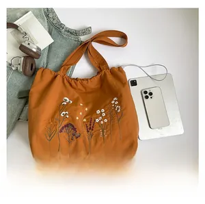 Macro detail of burnt orange canvas tote bag showing floral embroidery and texture