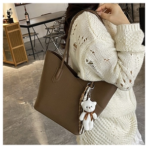 Braune Totebag aus Litchi-Leder mit weißem Bärenanhänger, am Model im Café gezeigt
