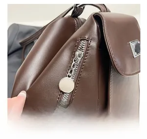 Close-up of smooth metal zipper and silver logo plate on dark brown leather backpack