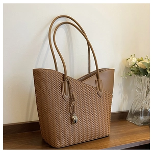 Detail of a brown woven texture tote bag with a golden moon pendant on a wooden surface