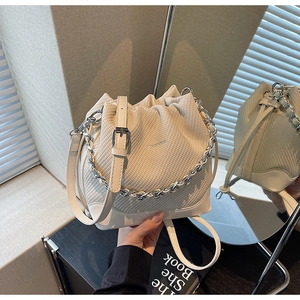 Detailed view of cream woven bucket bag with silver chain handle and brand logo