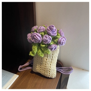 Close-up of handmade knit floral crossbody bag with purple roses on a wooden surface