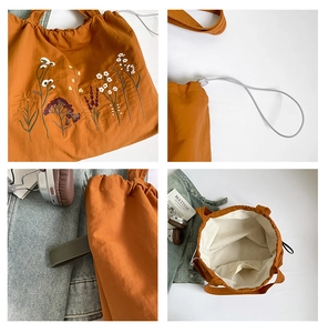 Detail view of orange canvas tote with floral embroidery and white drawstring closure