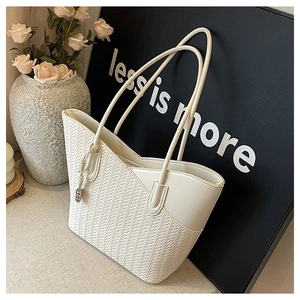 Detailed close-up of cream woven tote bag with smooth leather trim and metal charm