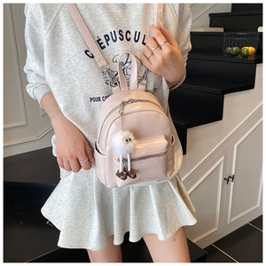 Detail of pink faux leather mini backpack with plush charm on a model in urban setting