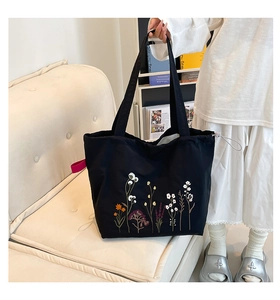 Close-up of floral embroidery and drawstring detail on this black canvas tote bag
