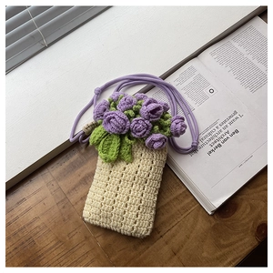 Close-up of handmade knit phone bag featuring purple crochet flowers on cream yarn