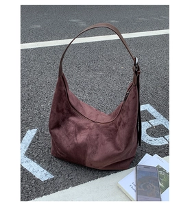 Detail of reddish-brown suede hobo bag with adjustable leather strap on pavement
