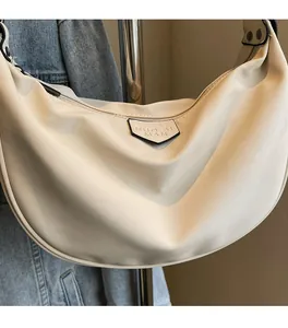 Detail of a creamy white crescent bag with a metallic logo plaque and smooth nylon fabric