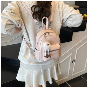 Rear view of a model wearing a mini light pink glossy backpack with a cute plush charm