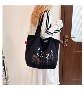 Detail of black tote bag featuring colorful wildflower embroidery and drawstring closure
