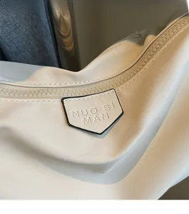 Detail of minimalist beige nylon bag featuring embossed logo and matching zipper closure