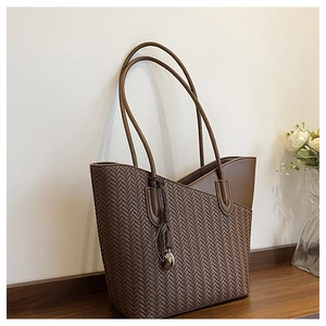 Detail of dark brown woven tote bag with silver teardrop charm on wooden surface