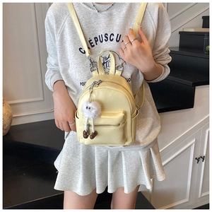 Mini cream yellow backpack with white plush monster charm detail on a grey sweater model