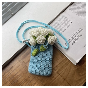 Close-up of light blue crochet mini bag with white rose floral detail on wood table