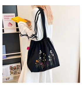 Detail of black tote bag with floral embroidery and drawstring closure on shoulder