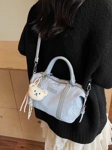 Light blue pleated tote bag with plush bear charm worn cross-body by a model