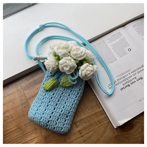 Detailed close-up of light blue hand-knit phone bag featuring white crochet rose accents