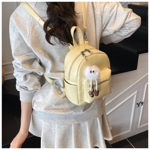 Close-up of yellow mini backpack with plush monster charm and adjustable leather straps