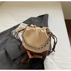 Close-up of woven drawstring bucket bag with leather base and silver chain detail
